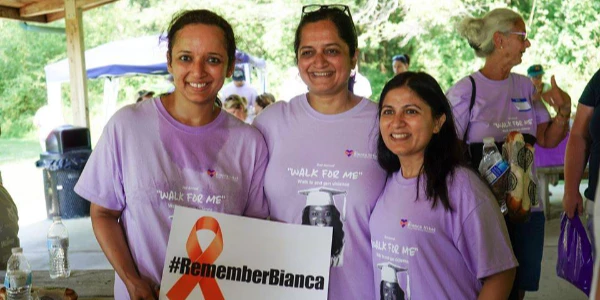 Three women wearing purple Walk for Me t-shirts and holding a #RememberBianca poster